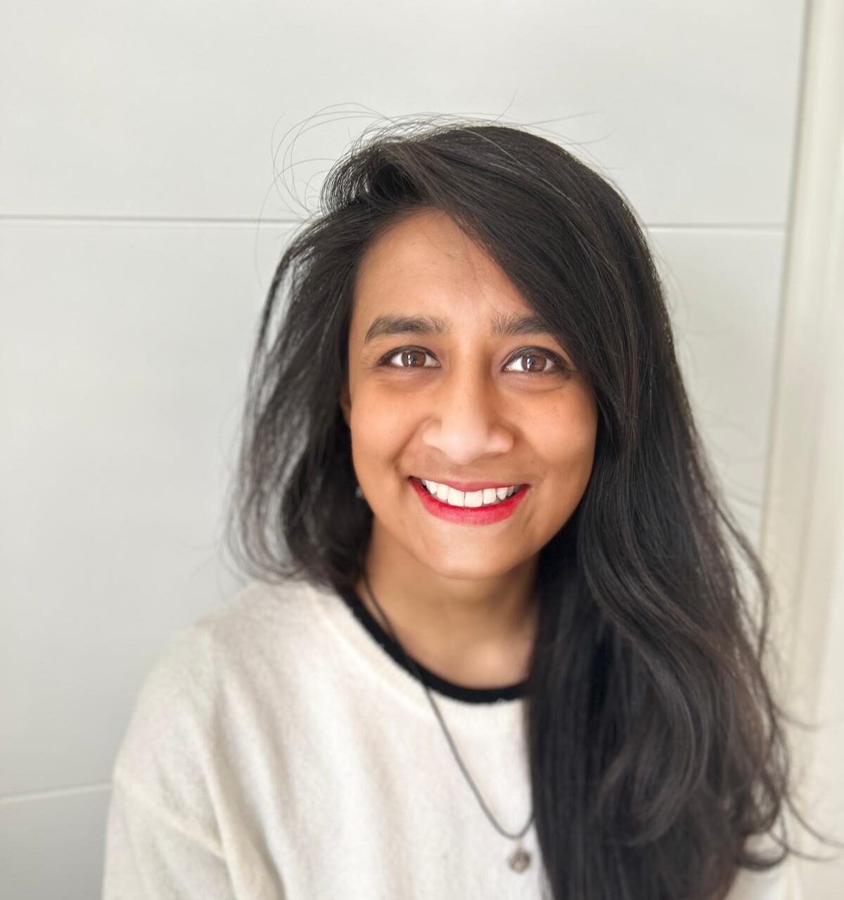 Madhuri Rahman has long, dark hair and wears a cream sweater with black trim and a pendant necklace.